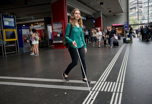 Une femme avec une canne d'aveugle à la gare. | © SBB CFF FFS/Flavia Trachsel